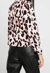 Blusa corta blanca con un audaz estampado de leopardo en negro y coral. Presenta mangas abullonadas y una cintura fruncida. Combinada con pantalones de cuero negros.