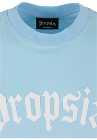 Lyseblå bomulds-sweatshirt med ribbet rund halsudskæring og hvid grafisk tekst med prangende detaljer. Mærket viser "Dropsize medium."