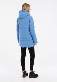 Blauwe pufferjack met een capuchon, voorzien van zijnaad en een ronde zoom. Draag het over zwarte leggings en stevige zwarte laarzen.