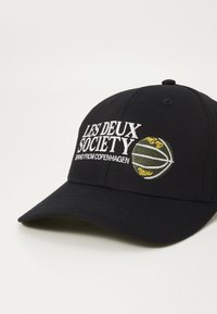 Fekete baseball sapka, pamutból készült. A fehér hímzett felirat „LES DEUX SOCIETY” található rajta, valamint egy zöld és sárga kosárlabdás grafika.