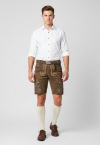 Bruna läderhosen med broderade blommönster, ihop med en vit skjorta med knappar, knälånga krämfärgade strumpor och bruna skor.