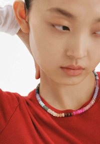 Collar de cuentas coloridas con cuentas redondas en varios colores, hecho de plástico translúcido. Lleva puesto un top de tela roja.