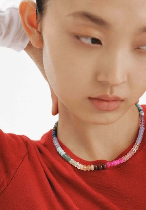 Collar de cuentas coloridas con cuentas redondas en varios colores, hecho de plástico translúcido. Lleva puesto un top de tela roja.