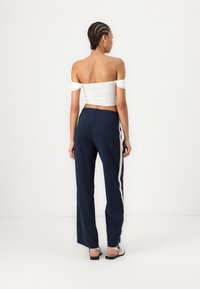 Crop top blanc décolleté et pantalon large bleu marine avec des rayures crème sur les côtés, bénéficiant d'une texture lisse et d'un design décontracté.