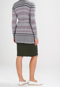 Gray and purple striped long cardigan with a belt; worn over a ribbed green skirt; white slip-on shoes; soft knit texture.