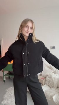 Svart kordfløyelsjakke i cropped design med høy krage, sølvfargede trykknapper og en teksturert overflate, brukt over et svart antrekk.