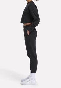 Felpa nera corta e pantaloni aderenti coordinati, con tasche, polsini a costine e leggeri accenti di logo, abbinati a calzature bianche.