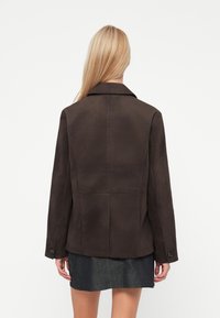 Brown suede jacket with a collar, slightly structured shape, and buttoned sleeves. Smooth texture, minimal seams, and plain design.