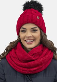 Berretto lavorato a maglia rosso con pom-pom in pelliccia sintetica nera e una sciarpa rossa coordinata, caratterizzata da un motivo testurizzato e un design piegato.