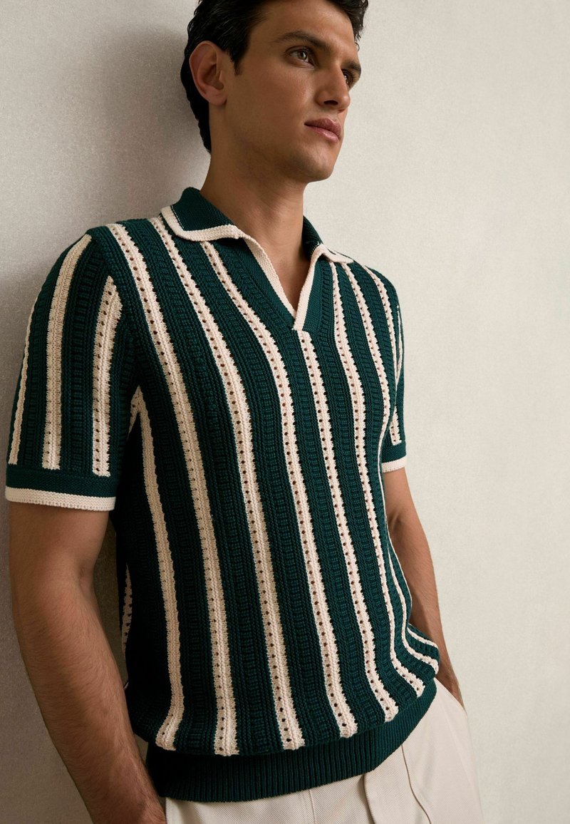 Polo en tricot avec des rayures verticales vertes et crème, à manches courtes et col en V. Tissu texturé avec une coupe ajustée.
