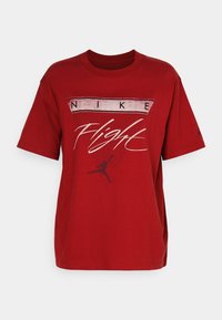 Červené bavlněné tričko s grafikou "NIKE Flight" a siluetou hráče v pohybu. Krátké rukávy a volný střih.