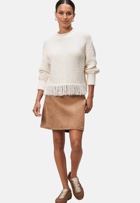 Creme gebreide trui met franjes aan de onderkant, gecombineerd met een bruine suède rok met zilveren studs. Compleet met bruine sneakers.