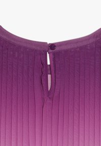 Lila ribbad tyg med en liten knappknäppning och nyckelhålsöppning vid bakre halsringning på ett plagg.