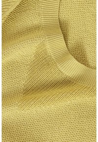 Gros plan d'un tissu tricoté jaune avec des motifs de points variés et un col rond côtelé.
