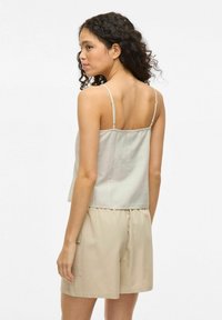 Top senza maniche grigio chiaro con spalline sottili, abbinato a pantaloni corti beige con tasca laterale e vita elastica. Tessuto morbido con una texture liscia.