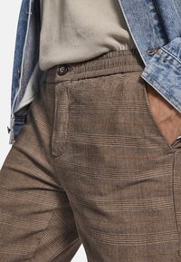 Bruine geruite broek van gestructureerde stof, met knoopsluiting, riemlussen en zijzakken.