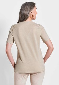 Beige Kurzarm-T-Shirt mit glatter Oberfläche. Rundhalsauschnitt und abgerundetem Saum. Getragen mit cremefarbenen Hosen, die einen lässigen Schnitt zeigen.