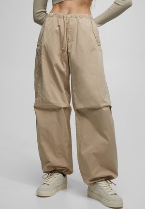 Beige loszittende cargobroek met elastische tailleband en trekkoord, gedragen met crèmekleurige sneakers en een cropped top met lange mouwen.