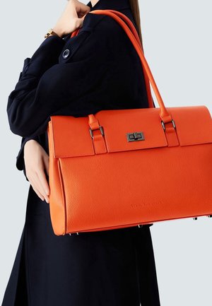 Orangefarbene Lederhandtasche mit klarer Form, ausgestattet mit silbernen Beschlägen, einem Schnappverschluss und zwei Griffen, getragen zu einem dunklen Outfit.