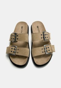 Braune Wildledersandalen mit zwei verstellbaren Riemen und silbernen Schnallen. Weiches Innenfutter und strukturierte schwarze Sohle. Flaches Design, offene Zehenpartie.