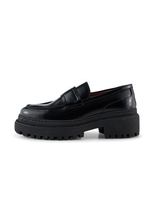 Mocasín de cuero negro con suela gruesa de tipo lug, tacón bajo y detalles cosidos, mostrado de lado sobre un fondo blanco.