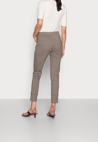 Pantalon marron fuselé en tissu doux avec une taille élastique et des ourlets retroussés, associé à un haut blanc ajusté et des sandales noires.