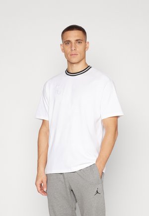 Hvid bomulds T-shirt med korte ærmer, en rund krave med sorte striber og et diskret logo foran. Bæres med grå sweatpants.