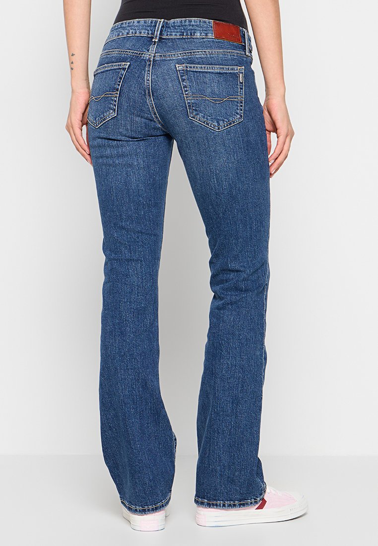 Helle Jeans mit ausgestelltem Bein in Dunkelblau mit strukturierter Oberfläche. Mit zwei Gesäßtaschen und einem braunen Lederpatch am Bund.