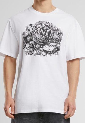 T-shirt blanc avec un graphisme noir d'un grand anneau du logo KANI entouré de montres, d'une voiture, de chaînes et d'autres petits objets sur le devant.