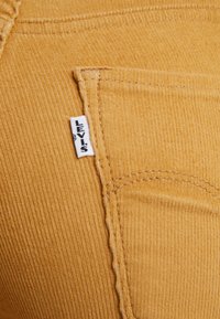 Tejido de pana en color mostaza con un bolsillo cosido y una pequeña etiqueta blanca de la marca Levi's adjunta a la costura del bolsillo.