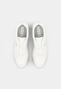 Baskets blanches avec une tige en cuir lisse, bout rond et coutures apparentes. Caractéristiques : lacets blancs, logo sur la languette et semelles intérieures grises.