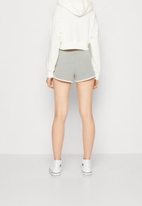 Osoba oblečená v bílé zkrácené mikině s kapucí, šedých sportovních šortkách s bílým olemováním a bílých vysokých teniskách Converse, stojící na neutrálním pozadí.