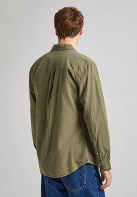 Olijfgroene shirt, lange mouwen, knoopmanchetten, zachte textuur, ontspannen pasvorm, rugplooi detail, gebogen zoom en subtiel verticaal streeppatroon.