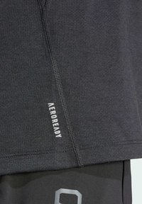 Camisa atlética negra con tela texturizada, que presenta detalles de costura y una etiqueta blanca "AEROREADY" en el costado. Adecuada para ropa de deporte.