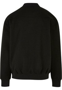 Sudadera negra con cuello redondo, mangas largas, puños acanalados y un dobladillo elastizado para un ajuste estructurado. Textura de tela suave.