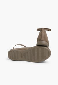 Zapatos de ante marrón con punta redonda, correa en el tobillo y tacón bajo. Suela de goma con un patrón texturizado para mayor tracción.