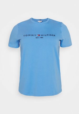 Lichtblauw T-shirt met korte mouwen met het "Tommy Hilfiger"-logo, een rood-wit-blauwe vlag en de tekst "EST. 1985" centraal op de voorkant.