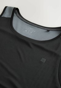 Débardeur athlétique noir avec doublure intérieure grise, étiquette taille moyenne et petit logo géométrique sur la poitrine.