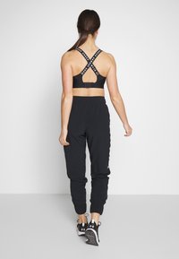 Svart sportbehå med korsade band, tillsammans med svarta joggers. Joggers har midjeband i elastisk resår och avsmalnande benslut.