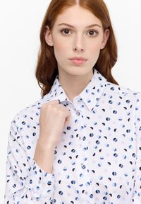 Camicia bianca con bottoni, decorata con un motivo di cerchi blu e rosa. Tessuto morbido con colletto strutturato e maniche lunghe.