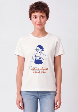 Femme aux cheveux courts et bruns portant un t-shirt blanc avec une illustration bleue d'une femme tenant une tasse de café et texte "Coffee is always a good idea."