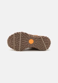 Suola di scarpe da trekking marroni con un motivo di battistrada testurizzato, caratterizzata da un accento circolare arancione al centro e due strisce orizzontali beige.