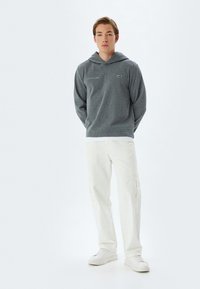 Sudadera gris con bolsillo canguro y capucha con cordón, combinada con pantalones cargo en color crema. Ambas prendas tienen un ajuste relajado y un diseño minimalista.