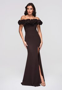 Braunes schulterfreies Kleid mit floralem Rüschensaum am Ausschnitt, figurbetonender Silhouette, Oberschenkelschlitz und glatter Textur; kombiniert mit transparenten High Heels.