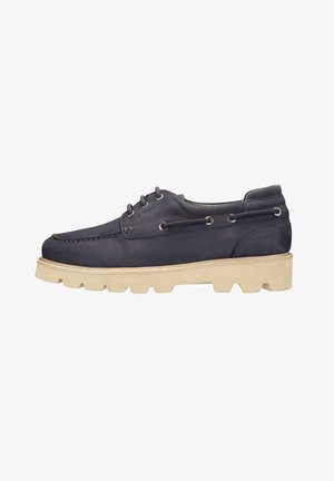 Chaussure bateau en cuir bleu foncé avec semelle crantée en caoutchouc beige et lacets à l'avant sur fond blanc.