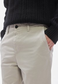 Lysebeige bomuldschinos med en lige pasform, udstyret med knaplukning og sidelommer. Stoffet har en glat tekstur.