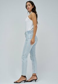 Jeans de tiro alto azul claro con un ajuste Slim, combinados con una blusa sin mangas blanca y tacones negros con tiras. Textura de denim suave, diseño clásico.