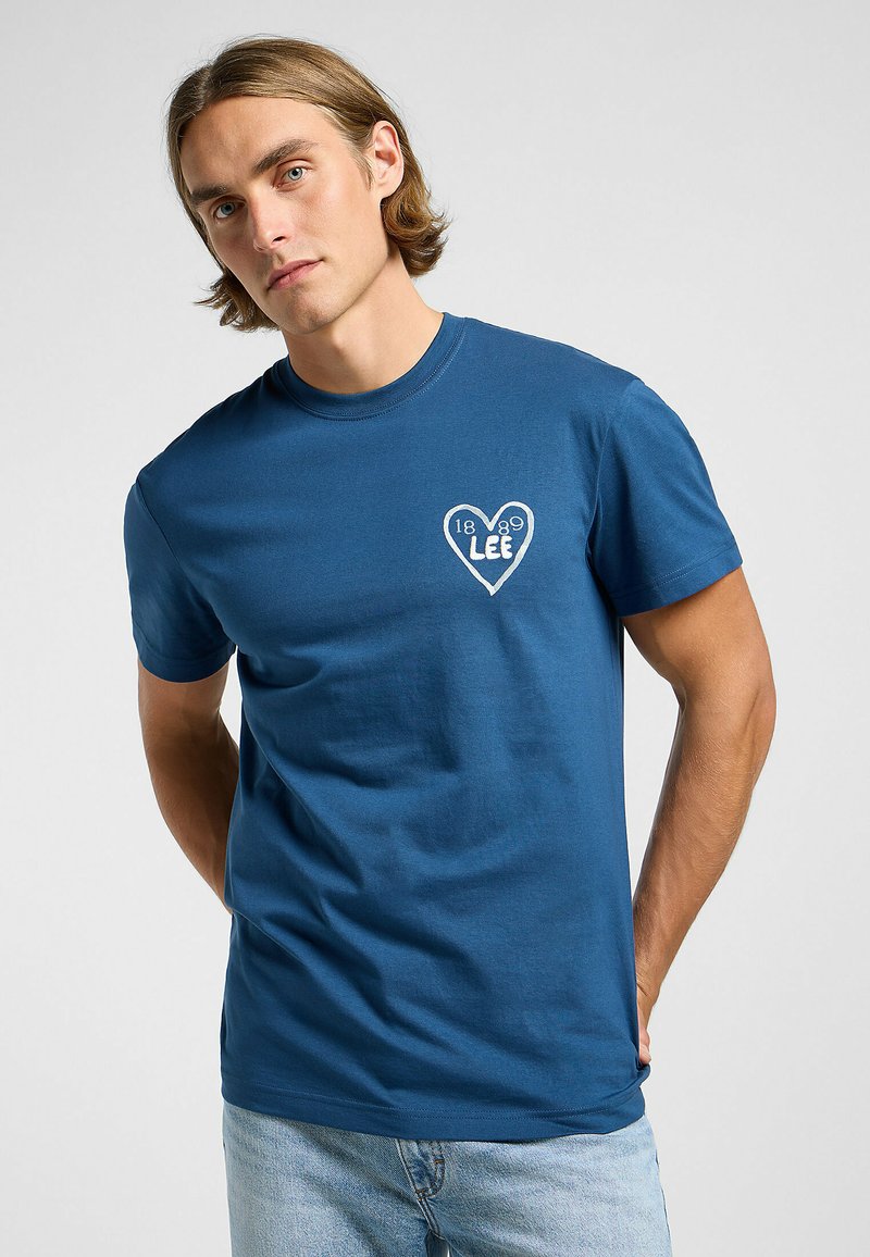 Blå bomulls-T-shirt med en vit hjärtdesign och texten "LEE" och "1889". Kortärmad och rundad halsringning. Enkel och avslappnad passform.