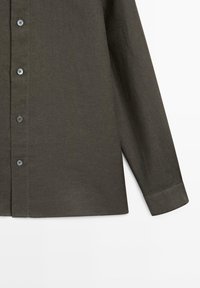 Mørkeolivengrøn langærmet skjorte med knapper og manchet, vist fra midt på overkroppen til håndleddet på en hvid baggrund.