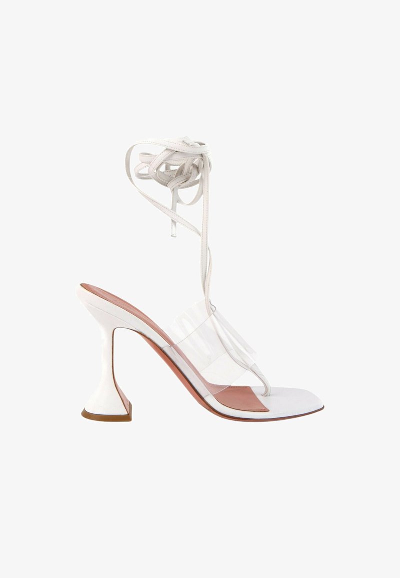Sandale blanche à talon haut avec bride transparente sur les orteils, design en boucle, lien autour de la cheville et talon évasé sculpté sur fond neutre.